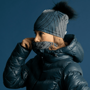 Big Fur Removable black pom beanie for women, side view of a woman putting her her abstract multifonctional tube to cover her face. 