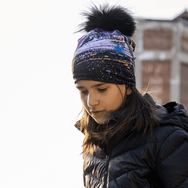 Young girl in profile, looking down and looking at the Abracadabra hat with detachable pompom illustrated by Mégane Fortin. This hat with abstract patterns is made of bamboo to wick away moisture. Perfect hat for hiking, walking, and outdoor activities. 