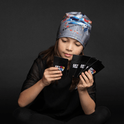 Girl wearing gray tuque with an abstract pattern with white, red, blue and yellow accents. Fit with everything! 