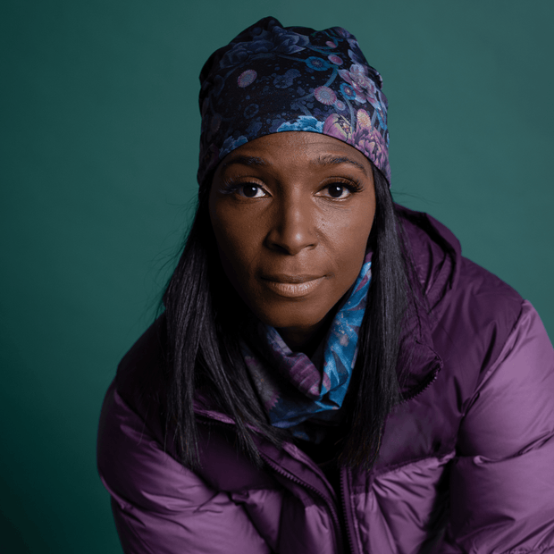 Photo of a black woman's face, wearing the Flora hat designed by Quebec artist Claire Anghinolphi. The woman has a sporty look and is wearing a purple down jacket. The Flora beanie is perfect for outdoor sports activities and can be worn with any outfit.
