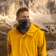Men hiking in mountains wearing the multi purpose neck warmer Movement Orange as a face cover to protect himself from the cold. Paired with a yellow jacket. 