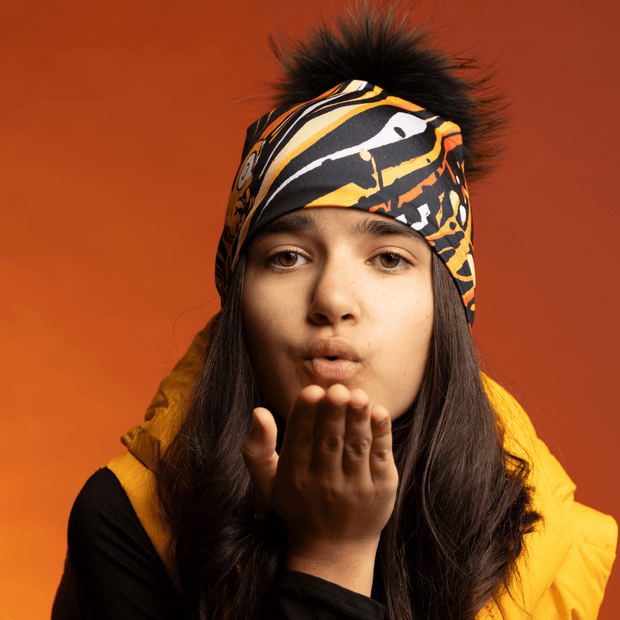 Teenager girl sending a kiss at the camera and wearing the Orange Owl beanie with pompom by Julie Rocheleau for the Lalita's Art Shop 24 collection.