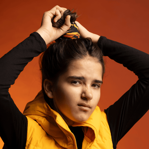 Teenager girl wrapping her Orange Owl multifunctional tube around her hair bun. Artwork by Julie Rocheleau for the Lalita's Art Shop 24 collection.