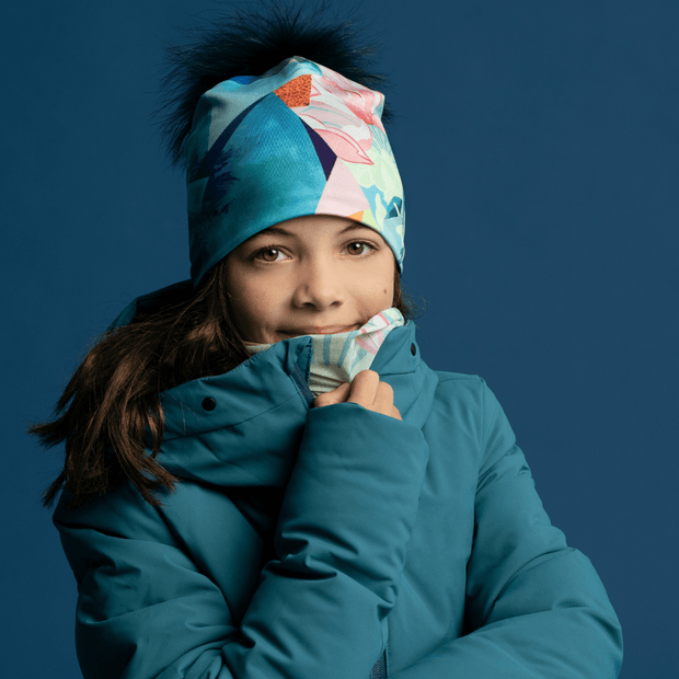 Close up of the girl wearing the Fleur PAstel pompom beanit hat with a beautiful teal jacket. Mix and match your favorite tuque with its multifunctional tube !