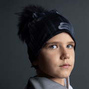 young boy with a sideways face wearing a snowborad and ski beannie hat designed by Zaire. The sport's beanie is in a black and grey tone with geometric shapes and a black pom-pom