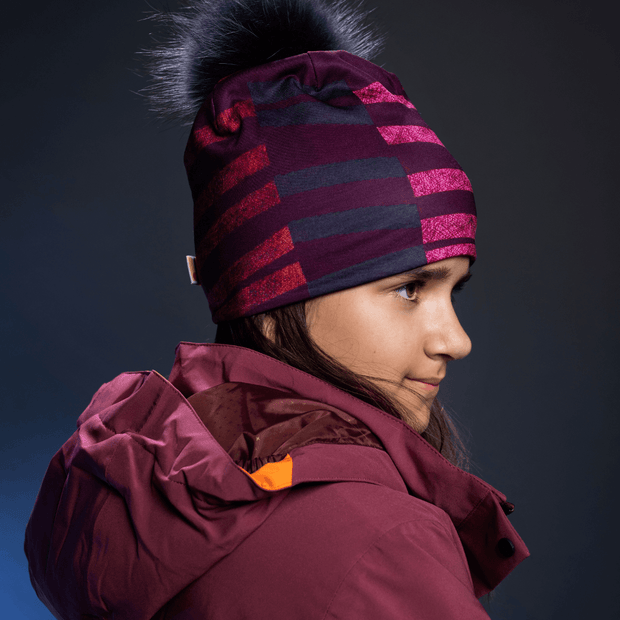 Girl, teenager, youth, wearing the purple, black and pink bamboo hat with a black fur removable pompom. Perfectly paired with a plum winter jacket. LAlita's Art Shop beanie designed by professional artist Valery goulet